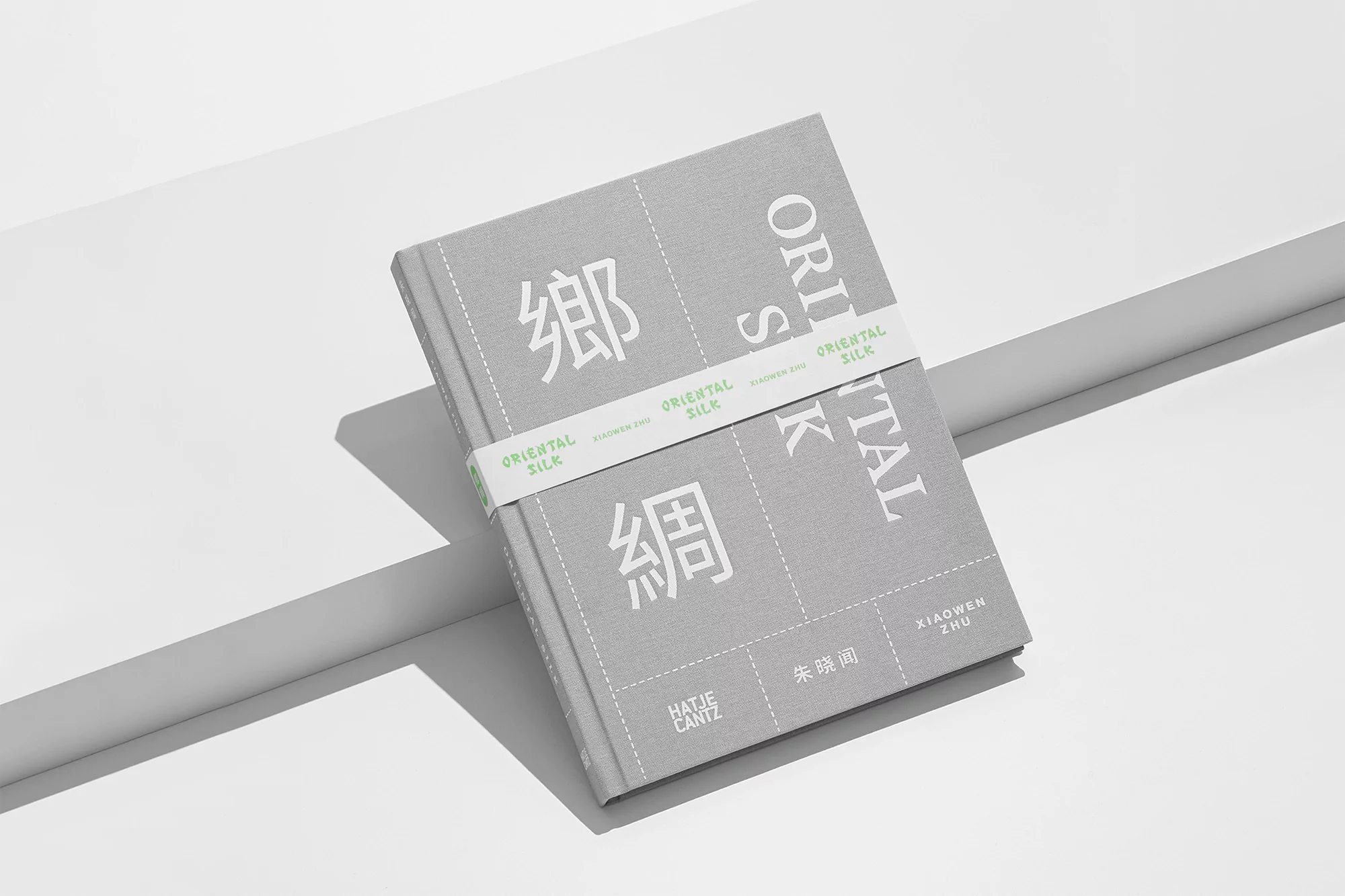 Grey hardcover book with white typographic cover design resting on a white geometric studio platform