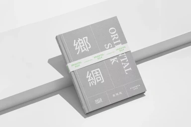 Grey hardcover book with white typographic cover design resting on a white geometric studio platform