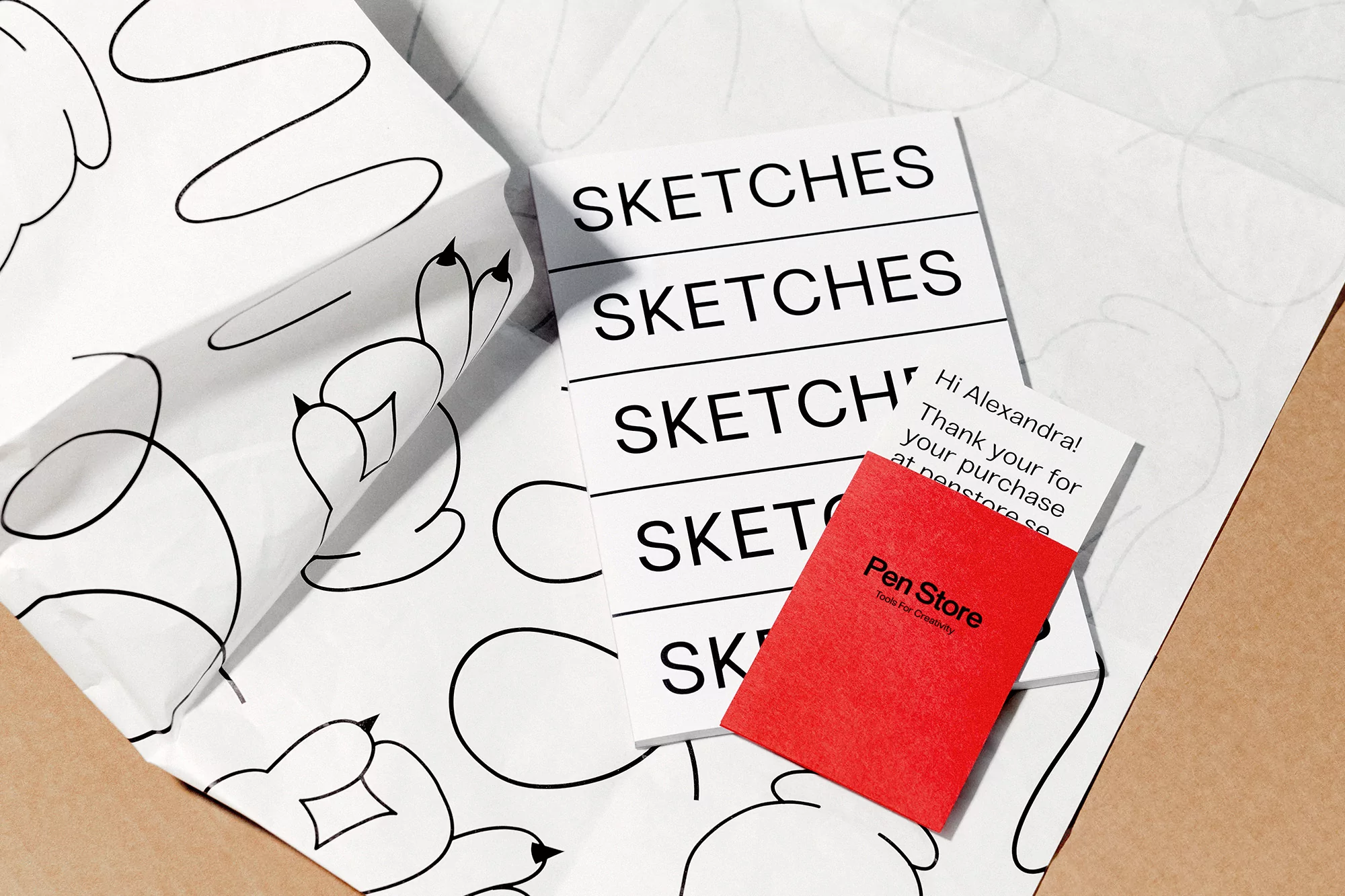Flat lay of sketchbooks, a Pen Store thank you card, and wrapping paper with black line art on a white background.