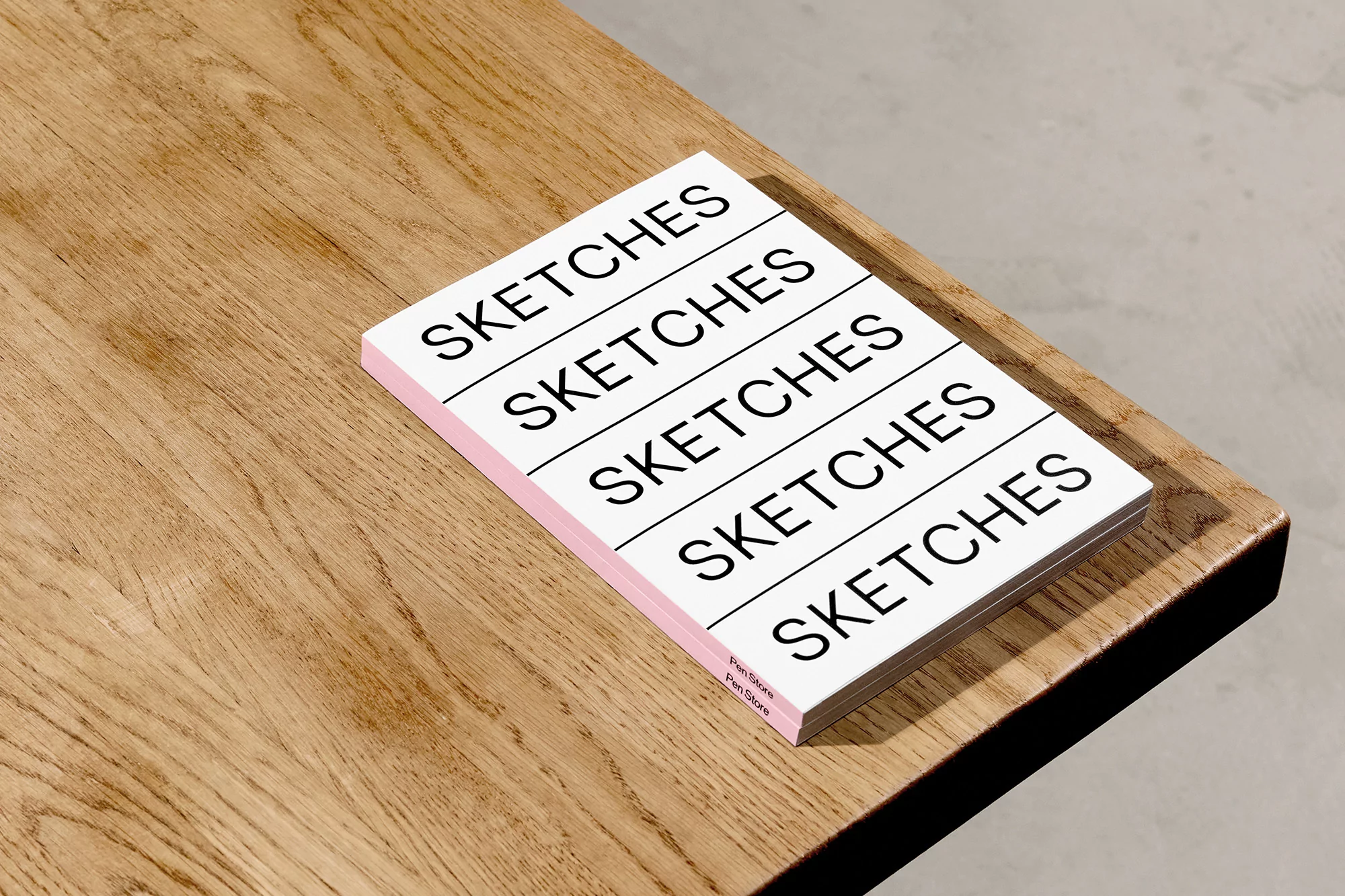 Stack of sketchbooks with the word 'SKETCHES' printed on a wood table against a neutral wall, top-down view, product photography.