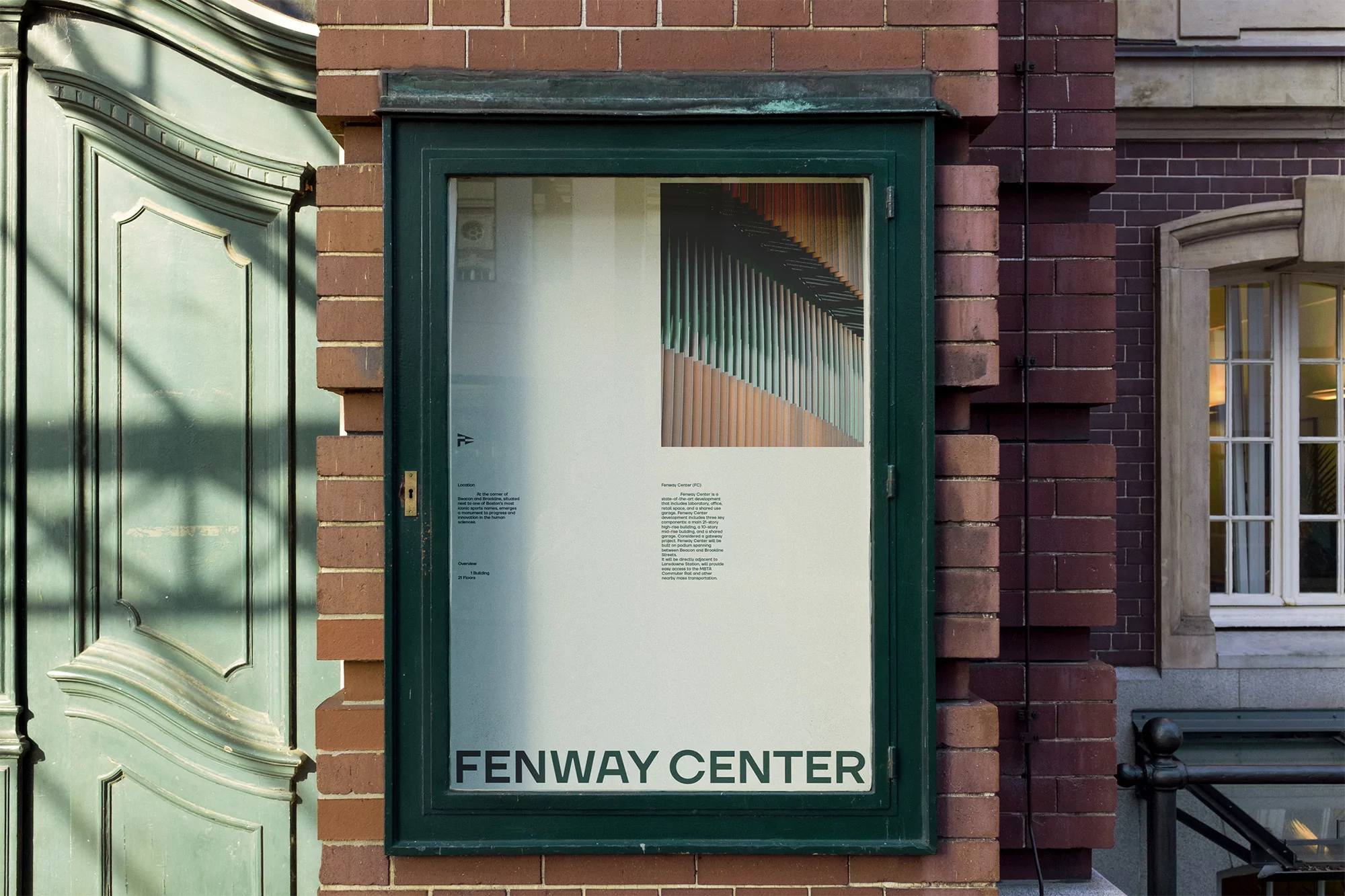 Fenway Center poster in a green frame, attached to a brick wall next to a teal door with architectural details. Window visible in background.