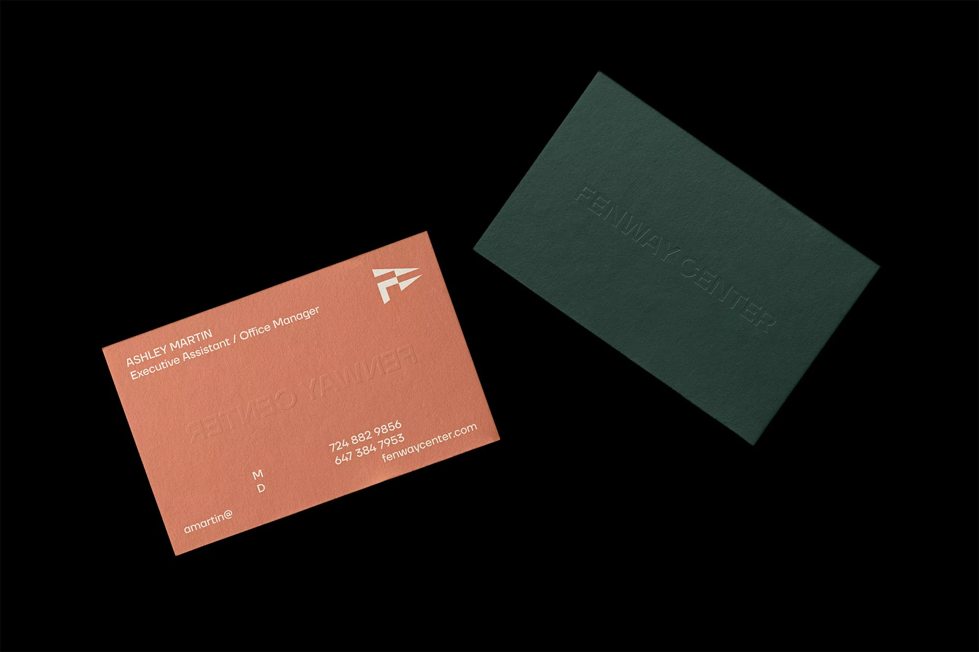 Two business cards, one peach-colored and one forest green, are angled against a black background, featuring the company name Fenway Center.