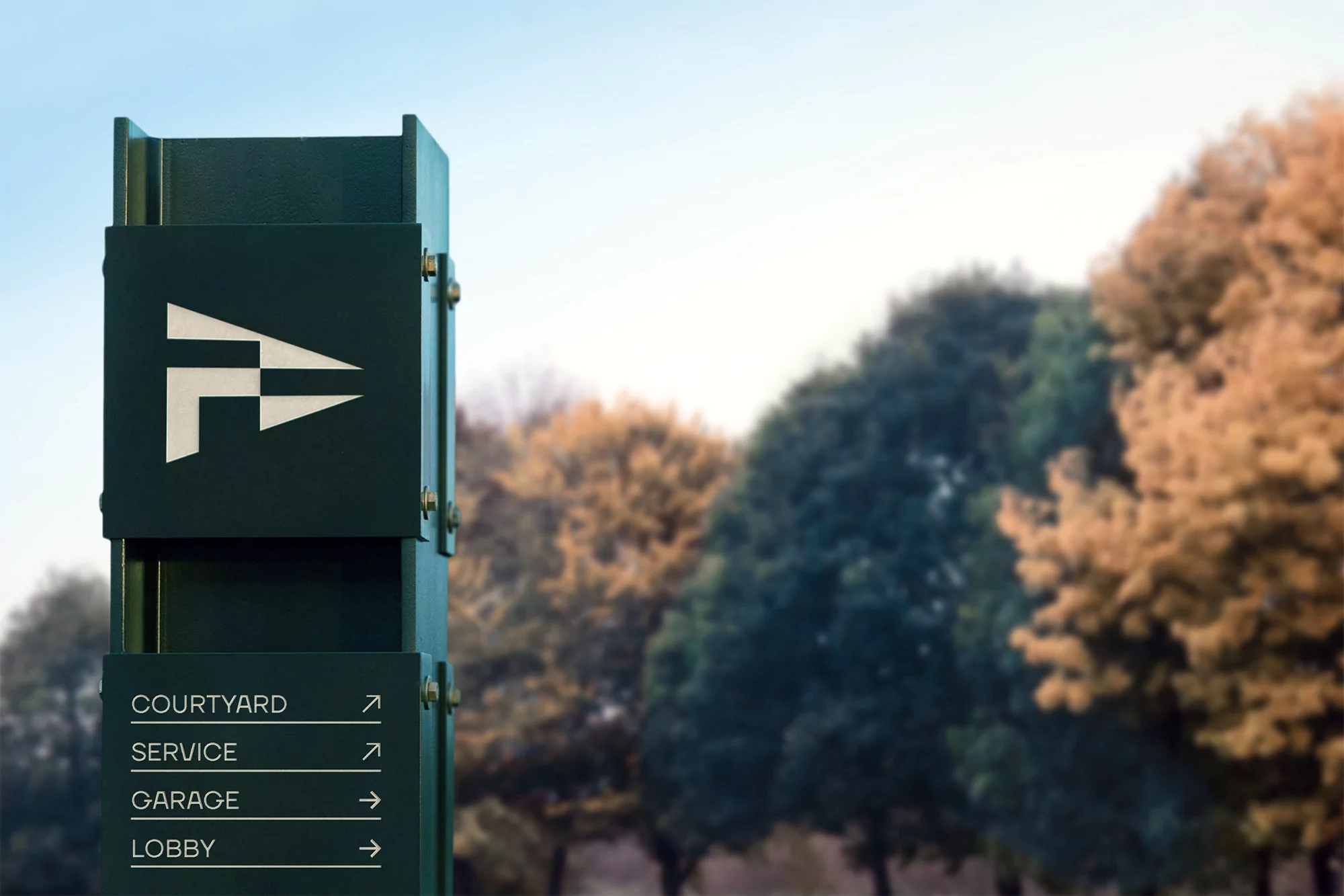 Directional signpost with white icons and text indicating courtyard, service, garage, and lobby, set against a backdrop of green trees.