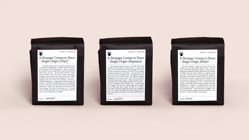 Three black coffee bags featuring different single origin roasts stand side-by-side against a neutral background, showcasing product design.