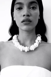 Close-up portrait of a woman wearing a chunky white statement necklace against a seamless white background