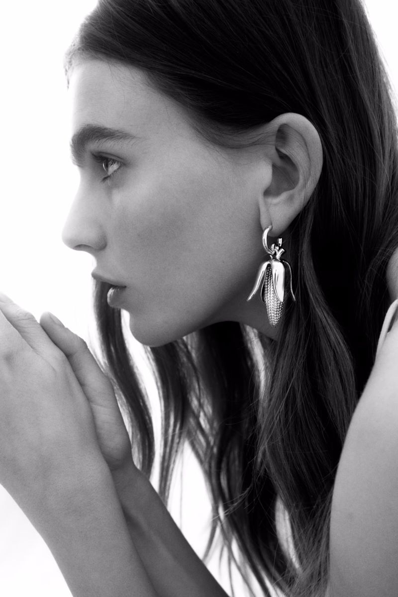 Close-up profile portrait of a female model wearing sculptural corn-shaped silver earrings for H&M summer 2025 campaign.