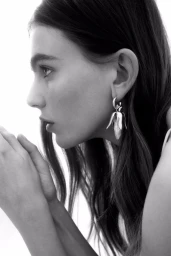 Close-up profile portrait of a female model wearing sculptural corn-shaped silver earrings for H&M summer 2025 campaign.