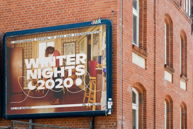 Billboard on a brick building advertising the 'Winter Nights 2020' performance festival, promoting ideas and experimentation during August.
