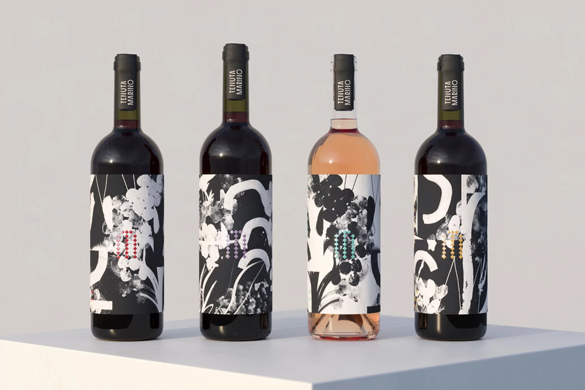 Four wine bottles with distinct black and white graphic labels stand in a row against a bright, neutral background, presenting a clean, modern aesthetic.