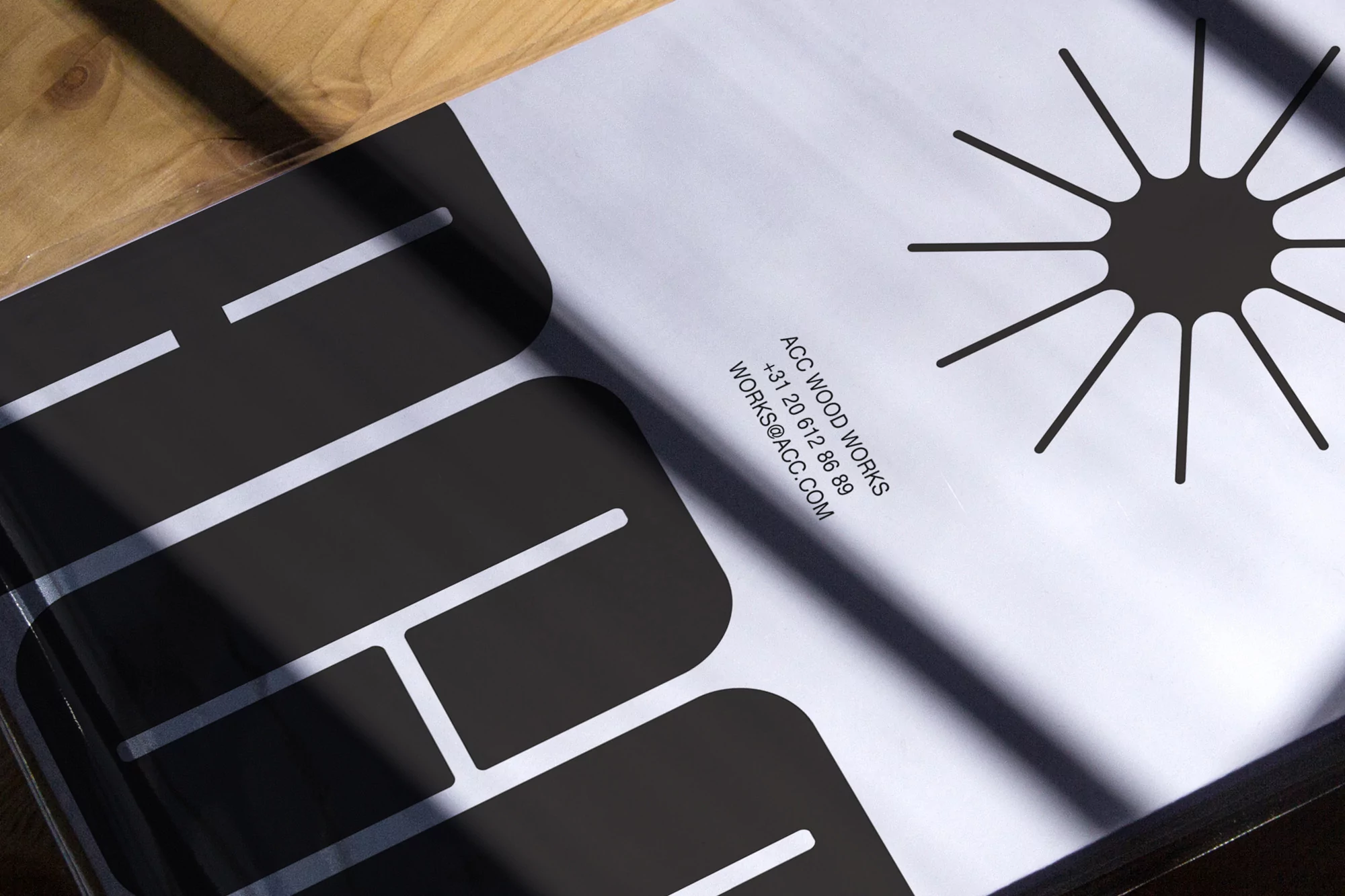 Close-up of a design book on a wooden surface featuring black graphic elements, company information, and strong shadows.