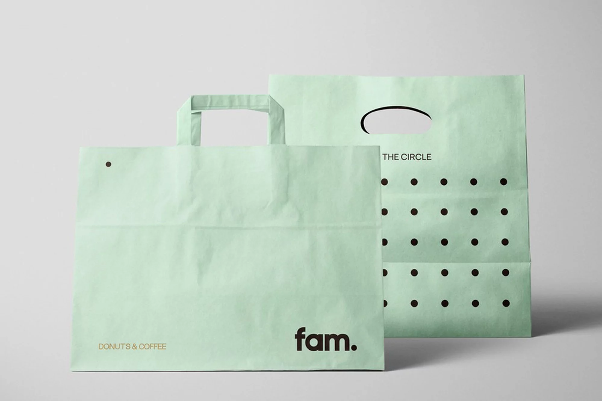 Two light green paper shopping bags with black logo and text on a gray background. Retail, branding, and product photography concept.