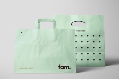 Two light green paper bags with printed branding against a neutral grey studio background