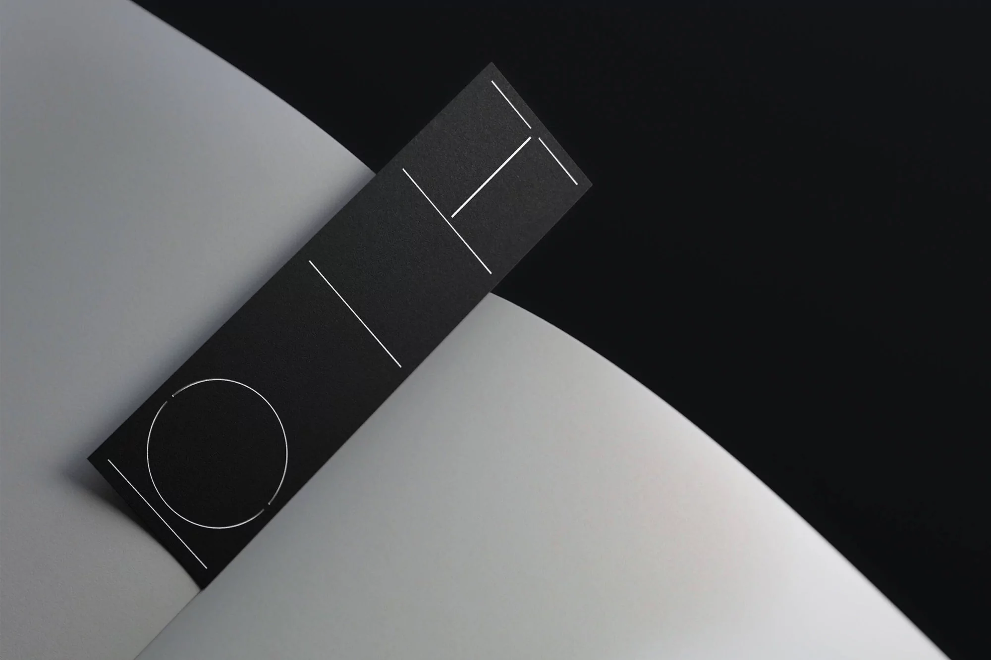 Minimalist product shot of a black rectangular card with white geometric design, resting on a white curved surface, set against a black background.