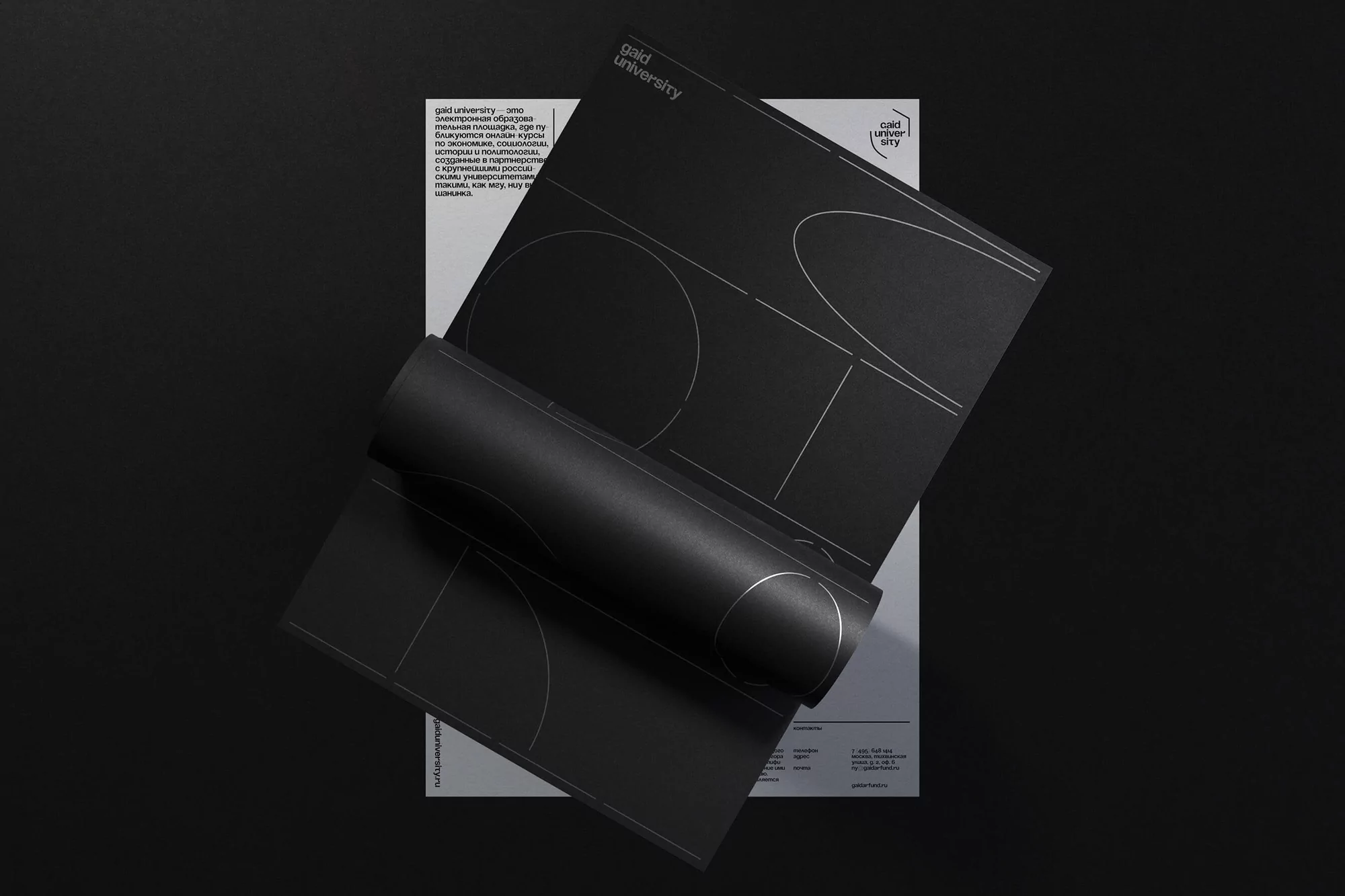 Abstract monochrome still life features black design document with geometric patterns atop grey brochure on a dark grey surface.