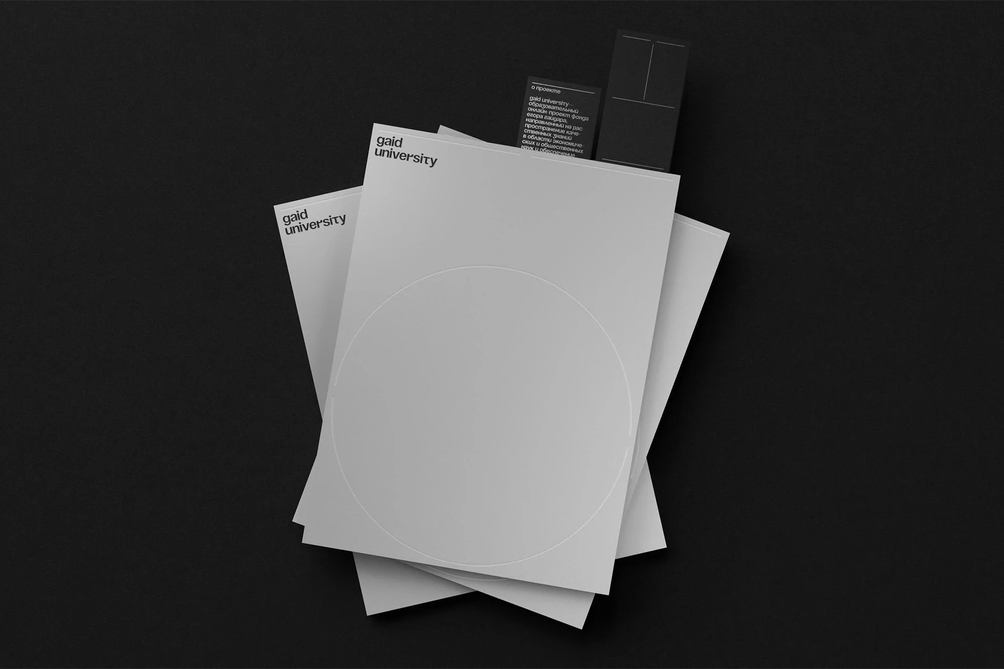 Overhead shot of Gaid University stationery on a black surface, featuring stacked flyers, brochures, and cards with minimalist design.
