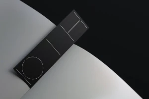 Minimalist graphic design identity card featuring white line geometric graphics on dark black paper against a curved white and black background