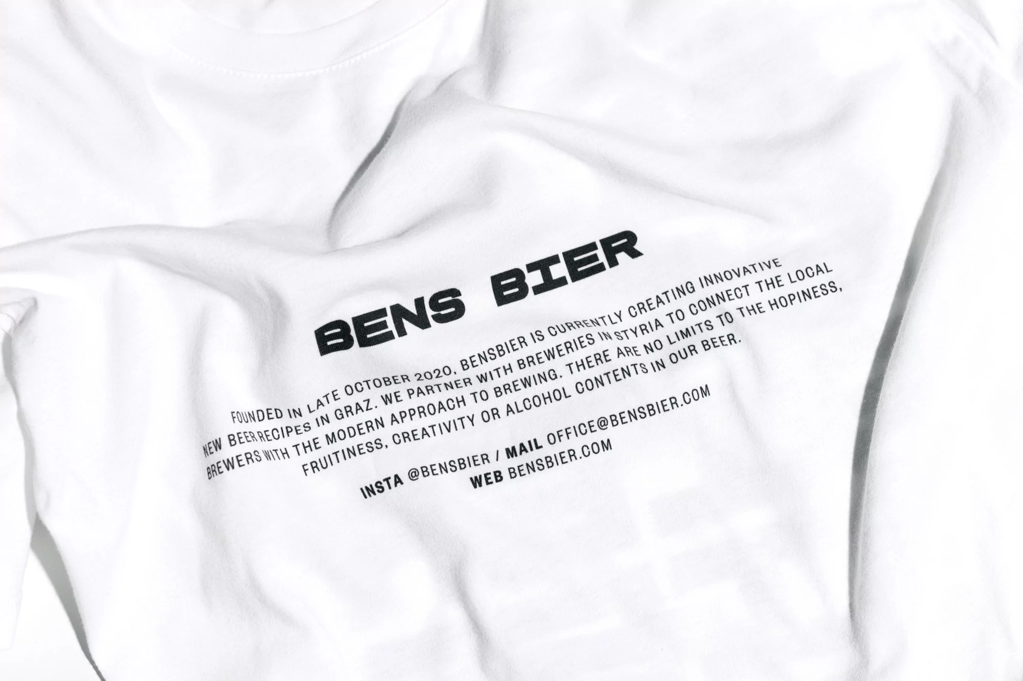 Close-up of a white t-shirt with black printed text 'Bens Bier', promoting a brewery, showcasing the brand name and company details.