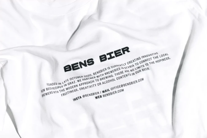 Close-up of a white t-shirt with black printed text 'Bens Bier', promoting a brewery, showcasing the brand name and company details.