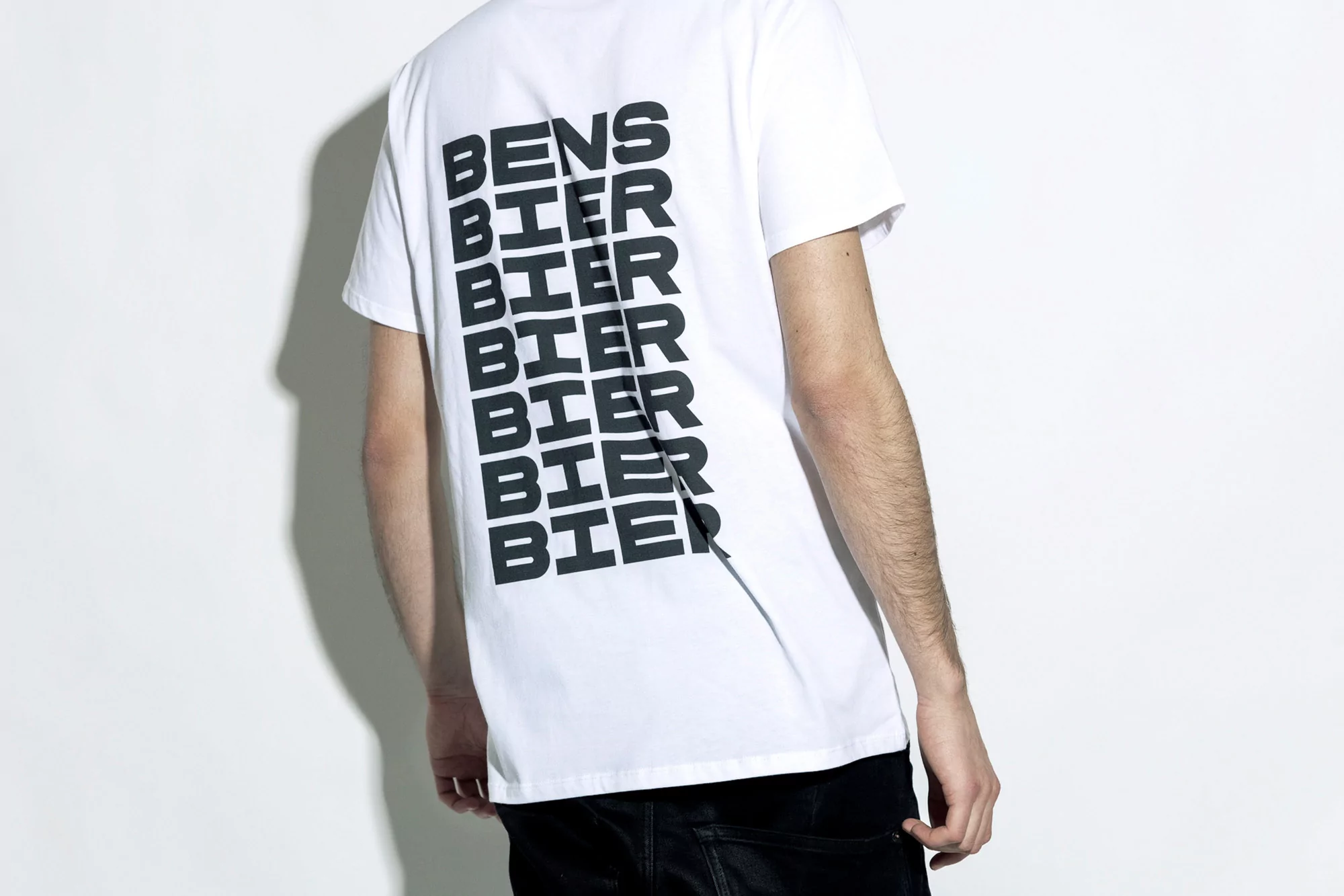 Rear view of an adult wearing a white t-shirt with black lettering against a stark white background, creating a minimalist aesthetic.