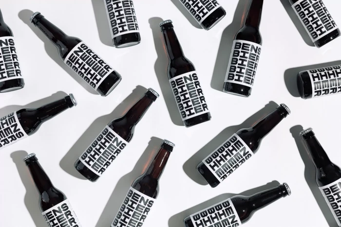 Top-down flat lay of multiple dark glass beer bottles with bold white typography labels arranged in a pattern on white surface.