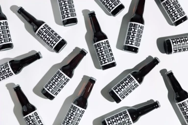 Top-down flat lay of multiple dark glass beer bottles with bold white typography labels arranged in a pattern on white surface.