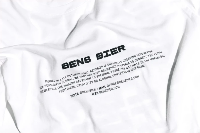 Close-up of a white t-shirt featuring black printed text branding for Bens Bier with descriptive brand narrative.