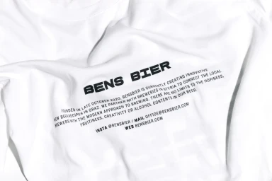 Close-up of a white t-shirt featuring black printed text branding for Bens Bier with descriptive brand narrative.