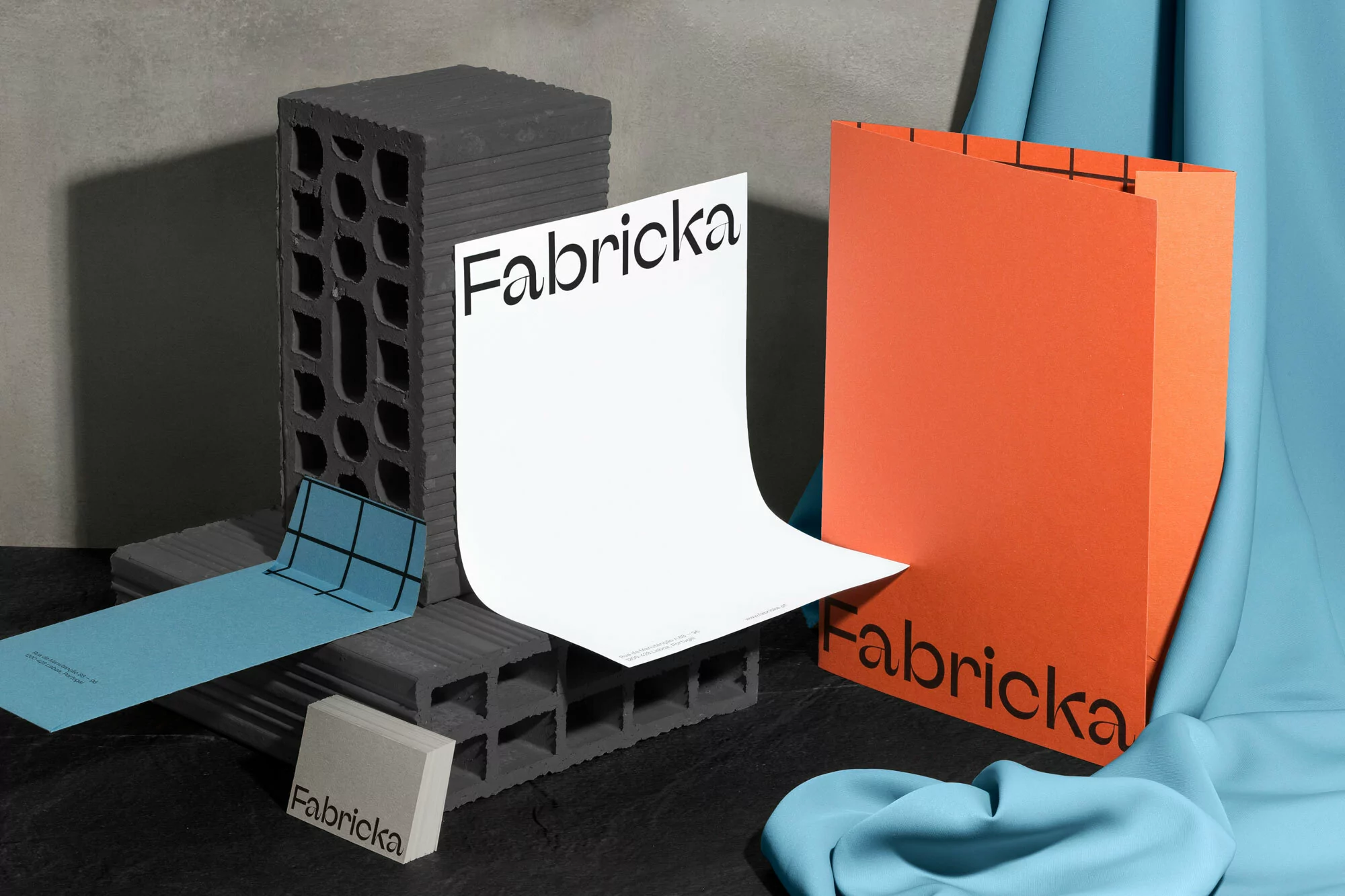 Stack of gray cinder blocks with product mockups featuring the brand 'Fabricka' in an indoor, studio setting with draped blue fabric.