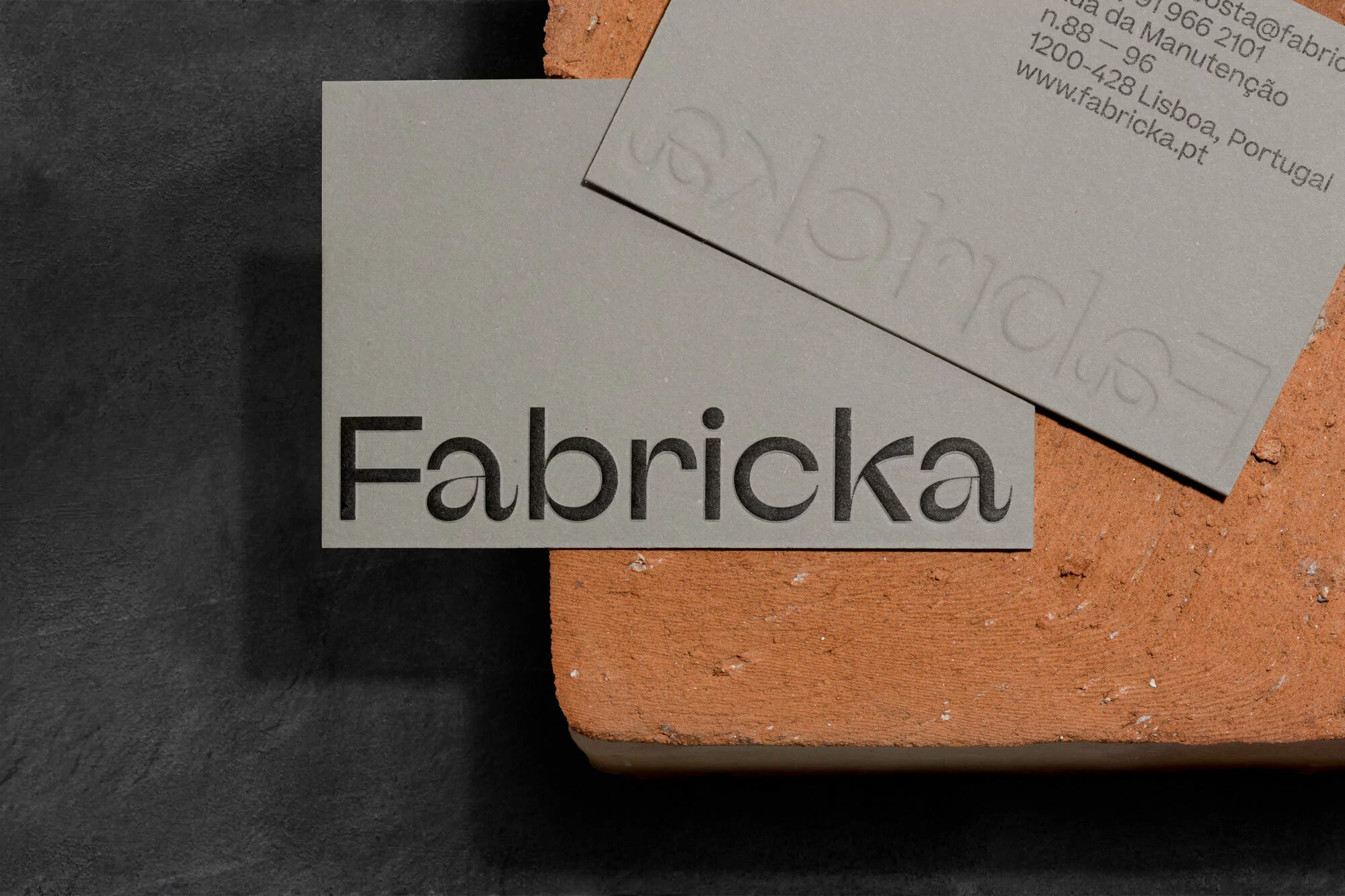 Elevated view of two gray business cards with black text atop an orange brick and dark gray textured surface in studio lighting.