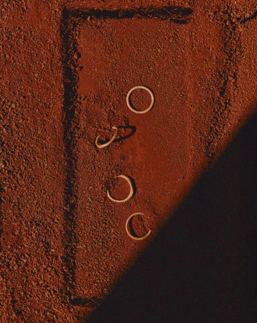 Aerial shot of three white rings and two partial rings on textured reddish-brown surface with rectangular line and shadows. 
