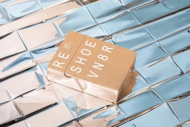 Brown branded product box resting on a reflective metallic crinkled foil surface.