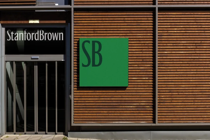 Exterior of commercial building featuring natural wood cladding, glass door with 'Stanford Brown' signage, and a green square logo.