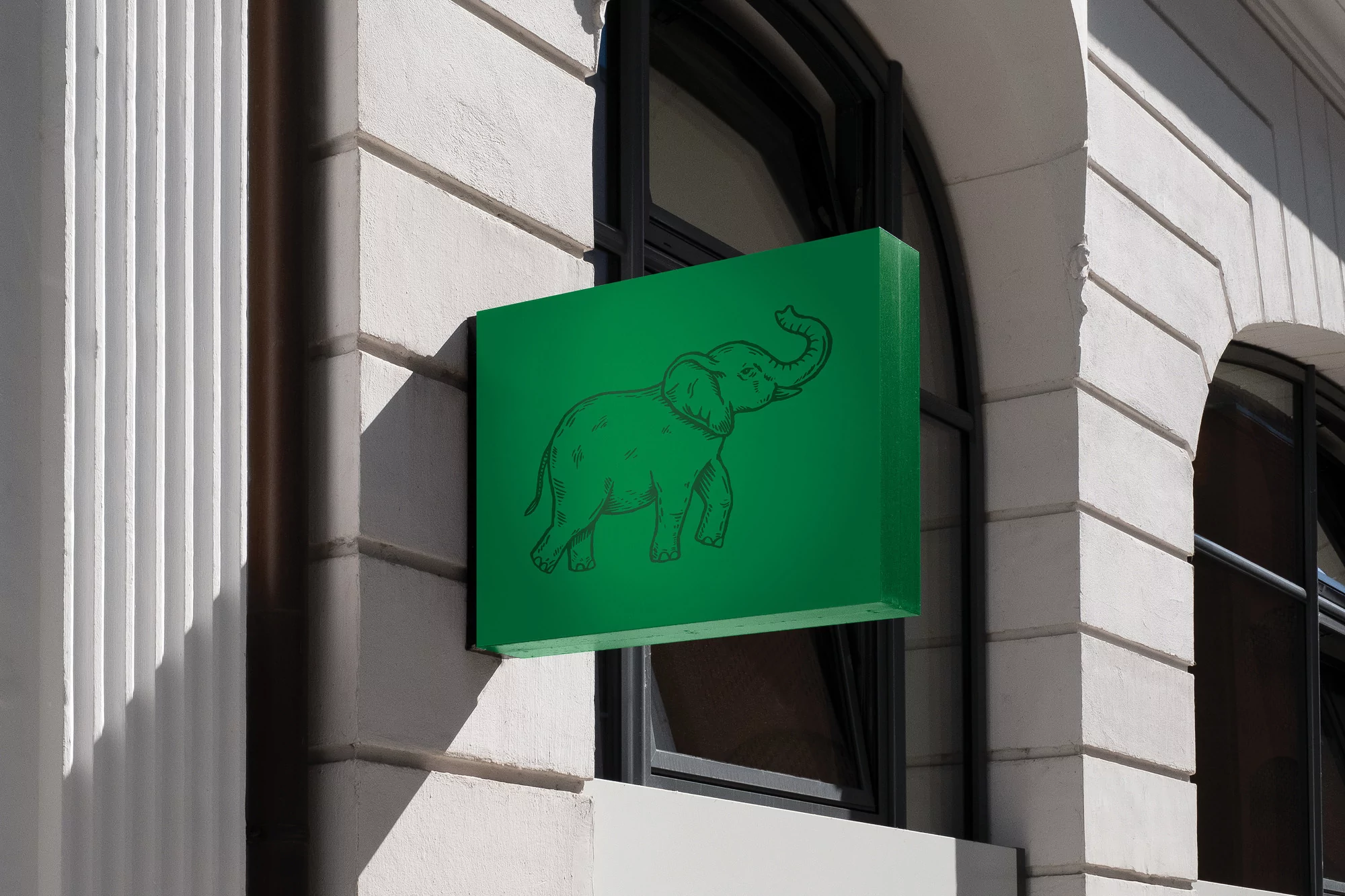 Outdoor shot of a vibrant green sign mounted on a white building featuring a sketched elephant illustration, set in an urban environment.