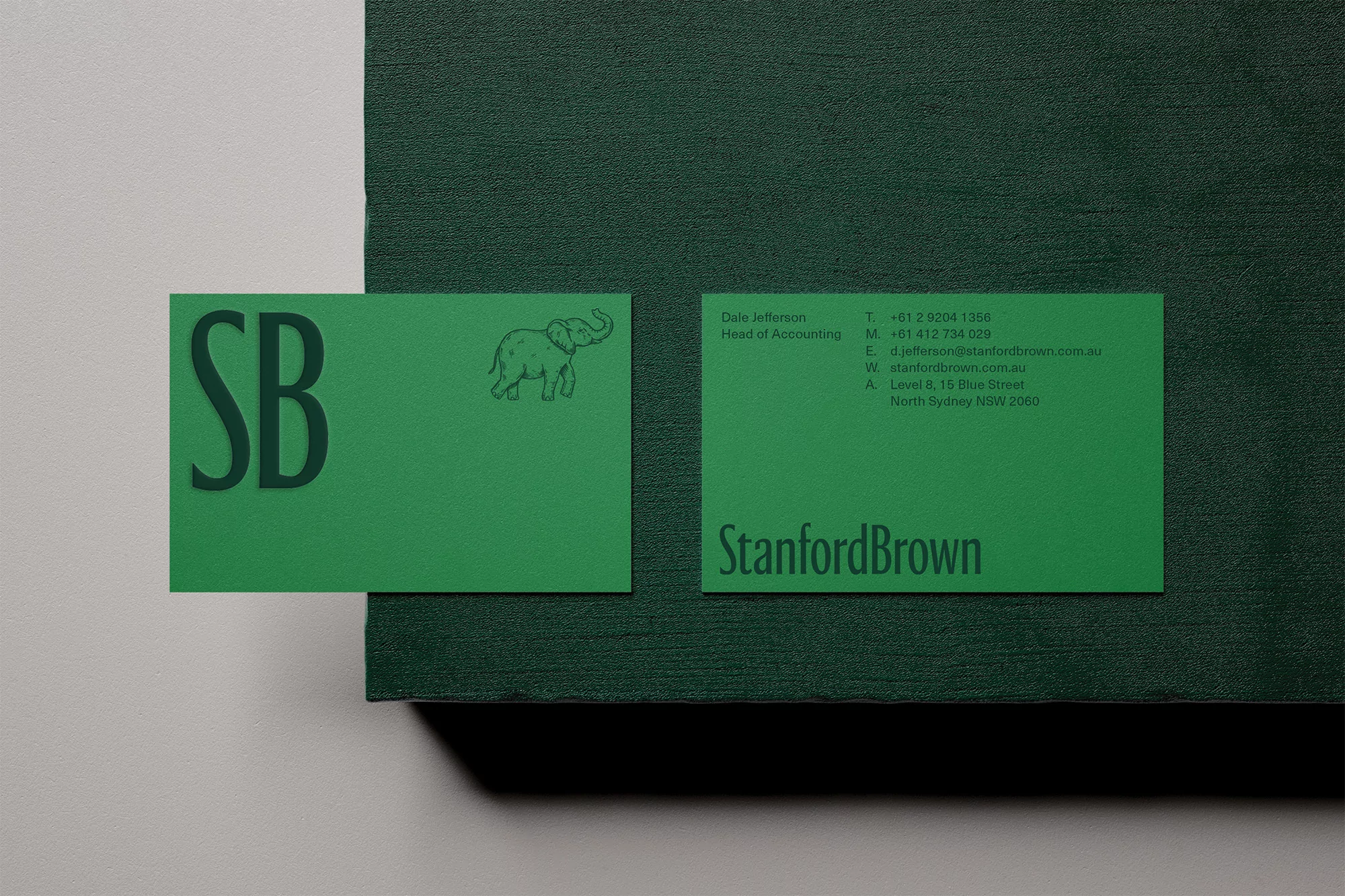 Two green business cards on a dark green surface, one featuring 'SB' and an elephant, the other with company and contact details.