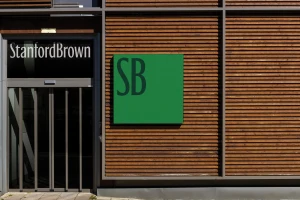 Building exterior featuring a wooden slat facade, glass entrance door with Stanford Brown signage, and a green SB logo square.