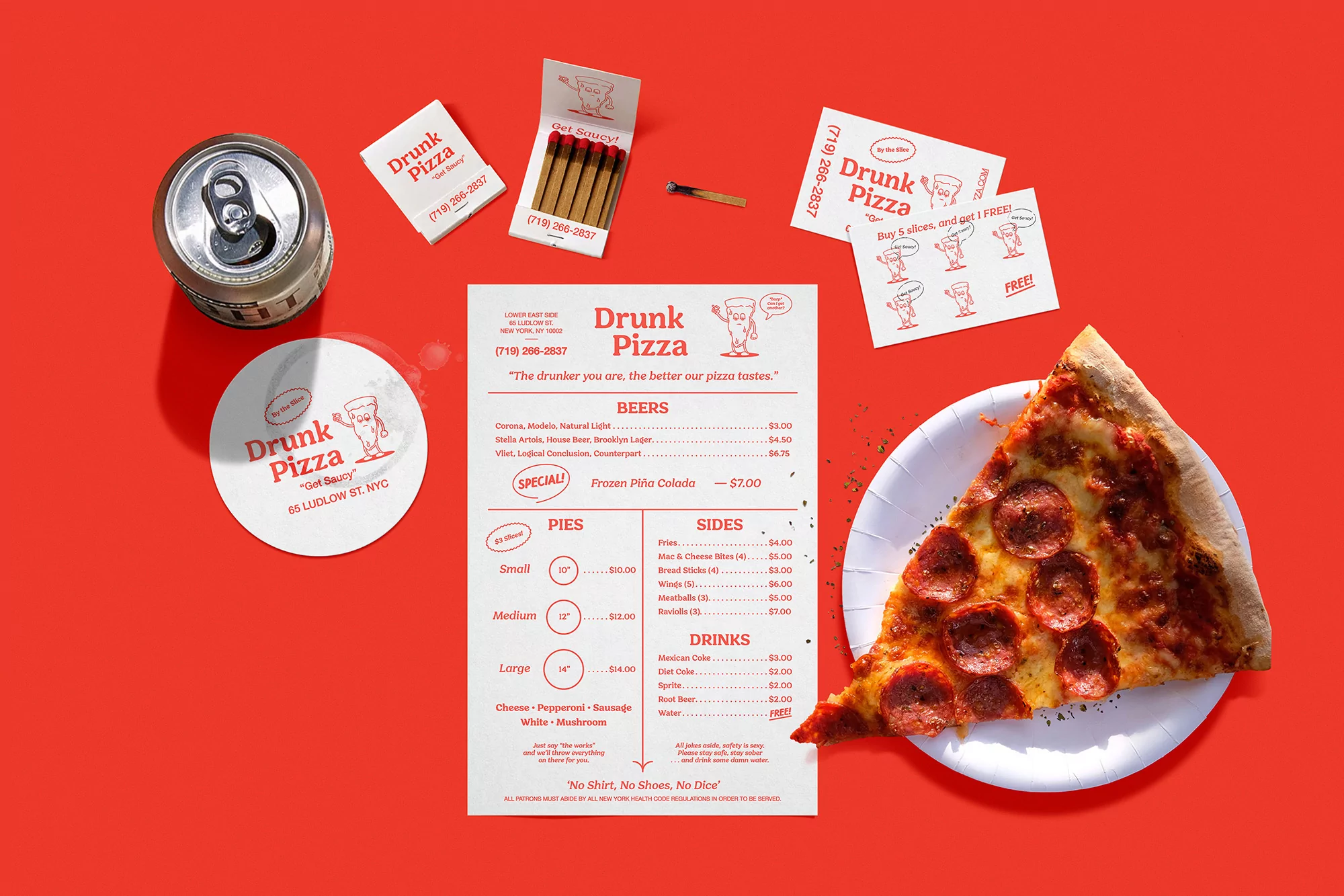 Overhead studio shot of a pizza slice, canned drink, and Drunk Pizza branded materials on a vibrant red background, promoting their NYC location.