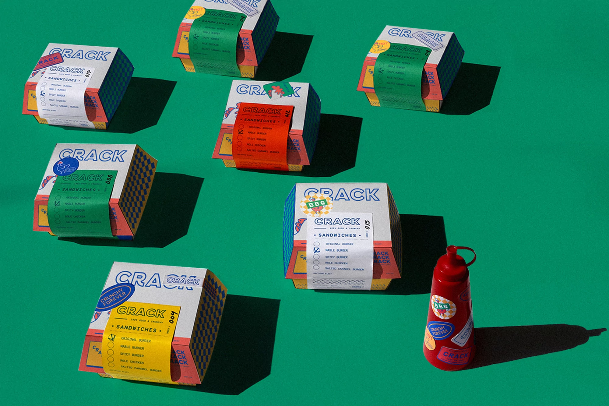 Eye-level, still life shot of burger sandwich boxes arranged on a green background, and a red ketchup bottle on the lower right.