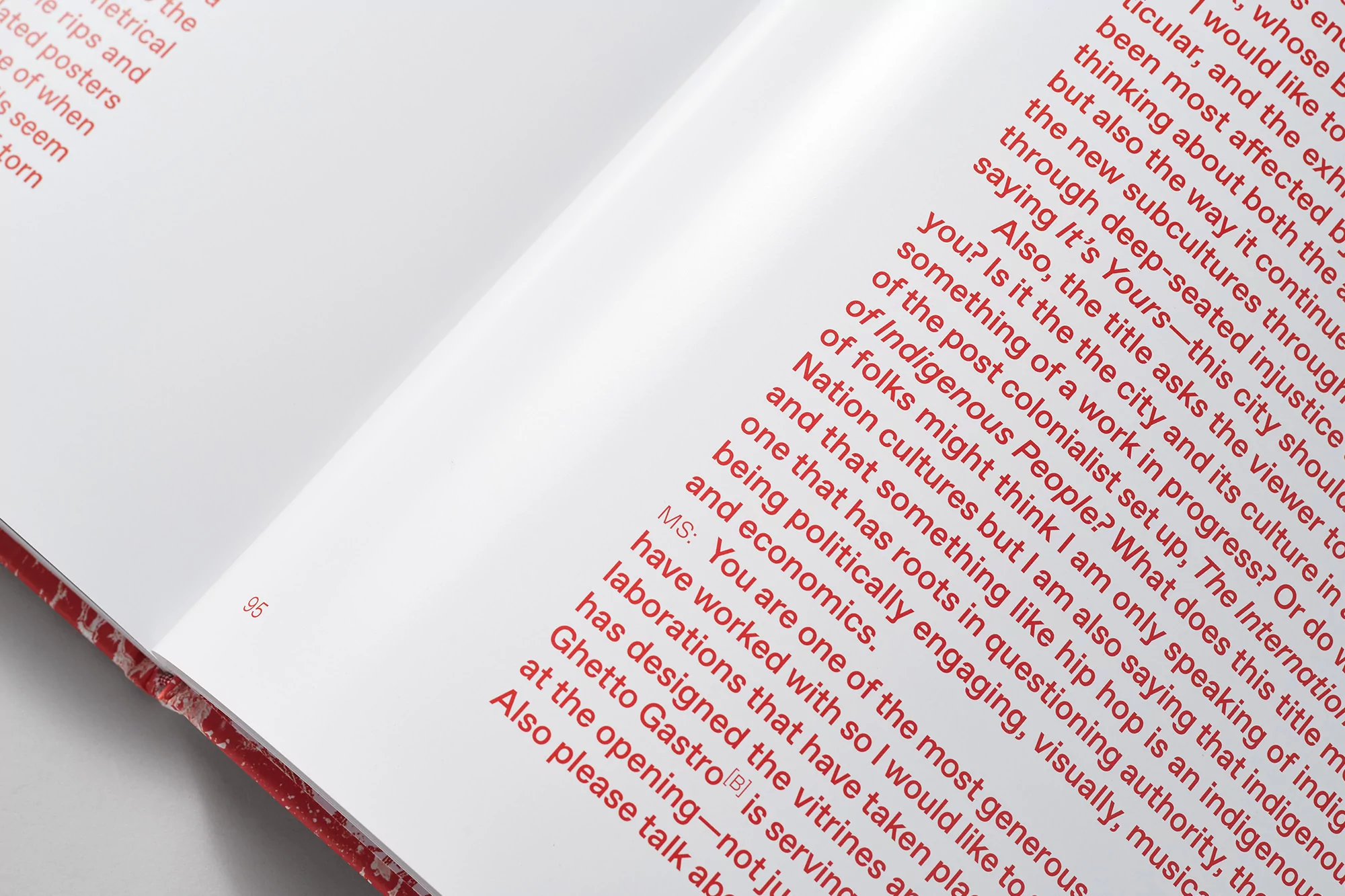 Open book displaying red printed text on white pages with information on art, culture, and economics, focusing on indigenous themes.