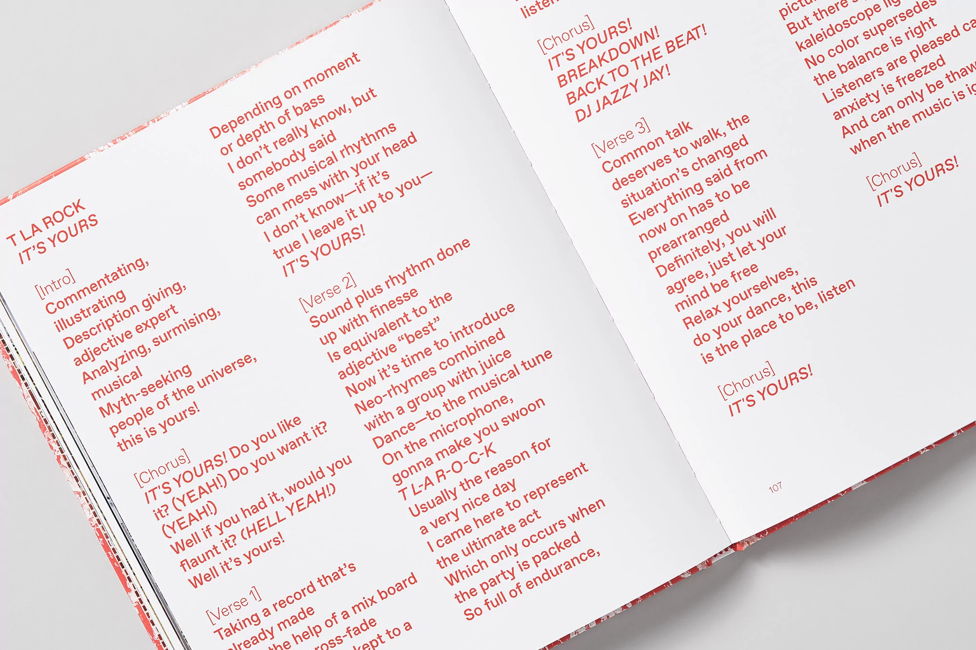 Open book spread showing red printed song lyrics on white pages set against a neutral background
