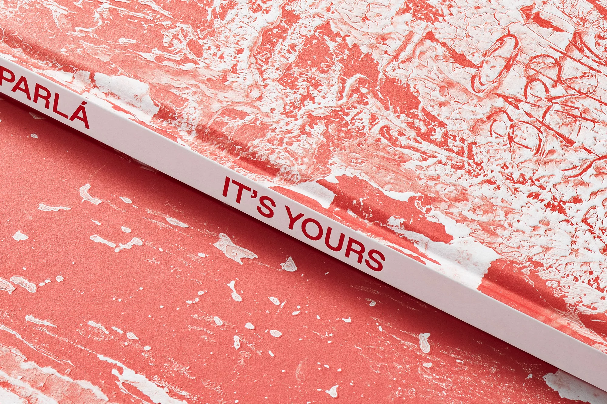 Close-up of a book cover featuring abstract white patterns on a salmon-colored backdrop, with the words 'Parla' and 'It's Yours'.