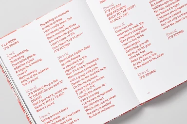 Open book spread showing red printed song lyrics on white pages set against a neutral background