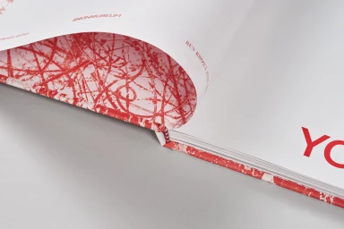 Close-up of an open hardcover art book with red and white abstract patterned pages and red typography on a grey surface.