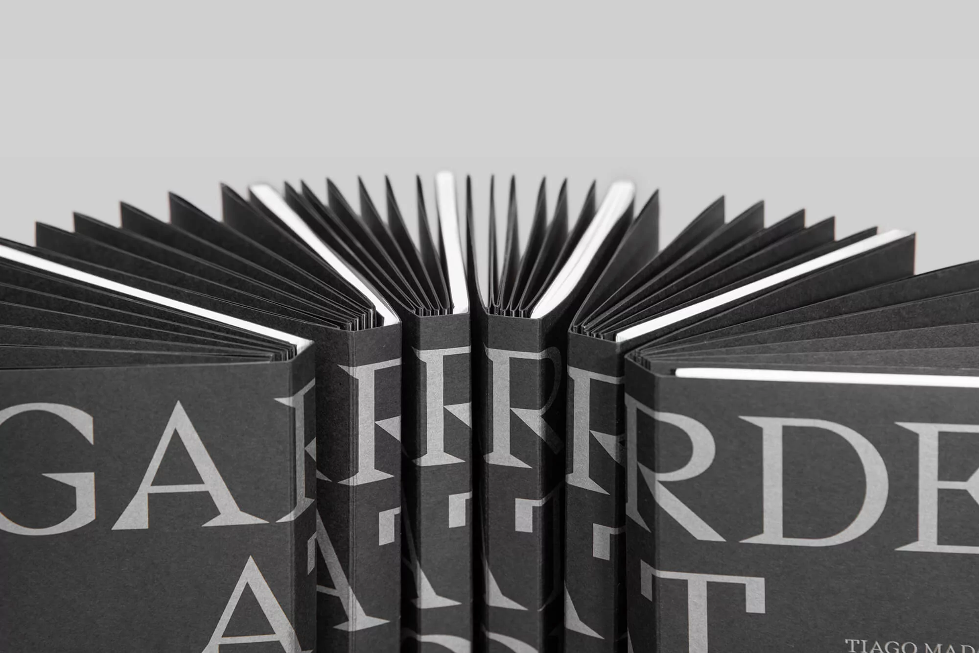 Overhead shot of black books, fanned open, displaying page edges and spine text against a neutral grey background, studio lighting.