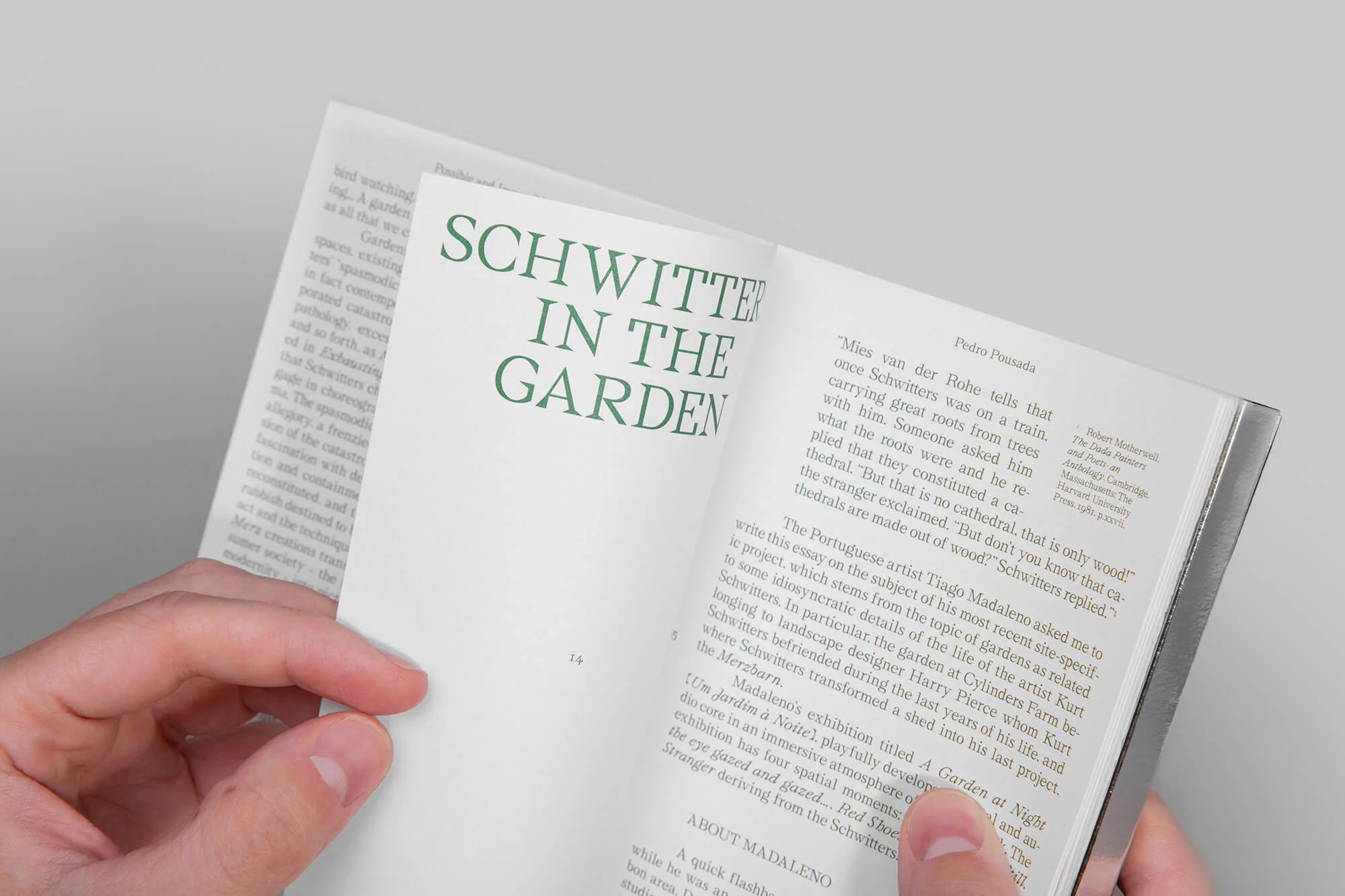 Open book featuring text 'Schwitters in the Garden' being held by hands, capturing a close-up view with a neutral background.