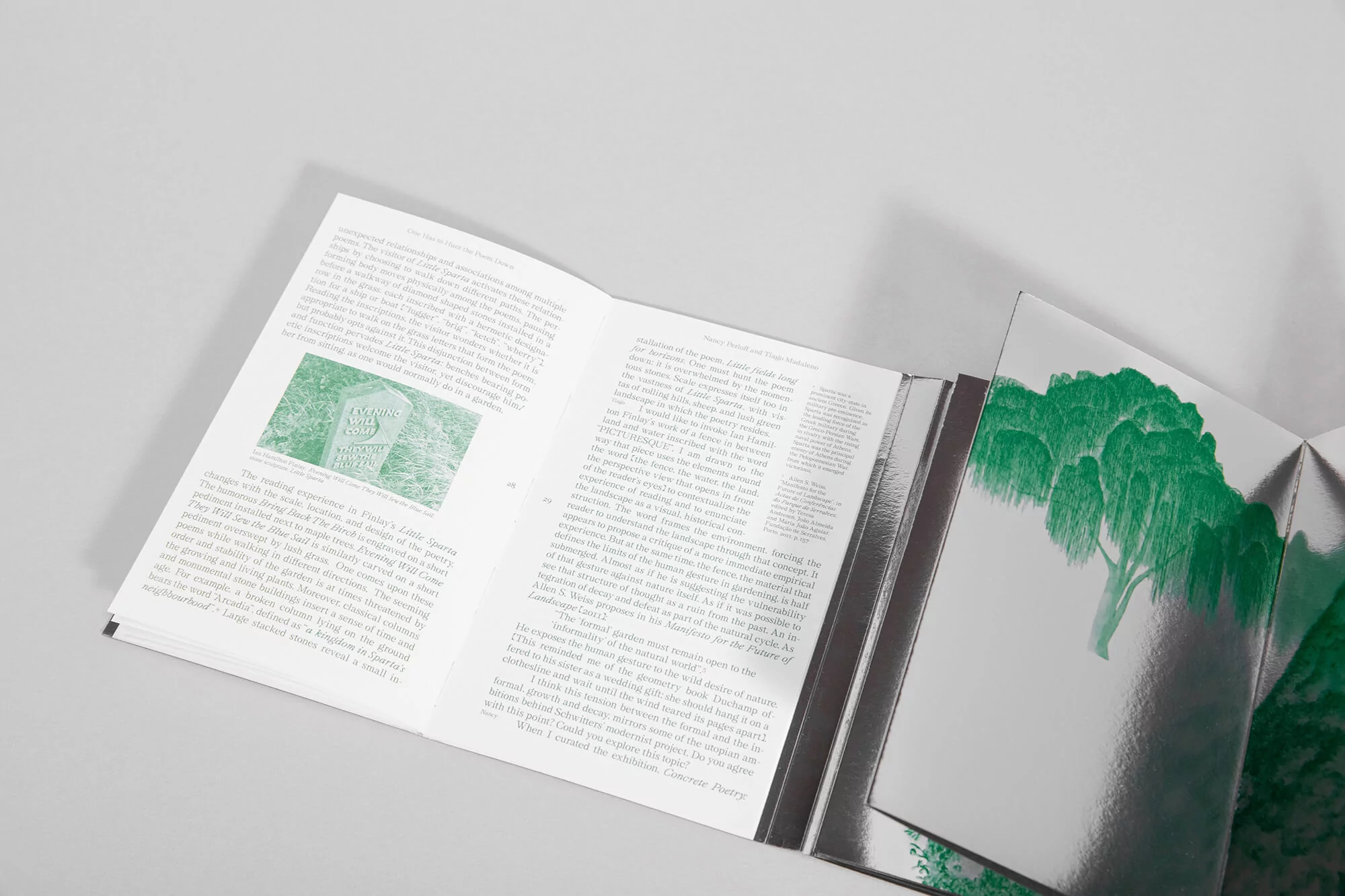 Open book displaying text and green artwork on a reflective surface, photographed indoors with soft lighting.