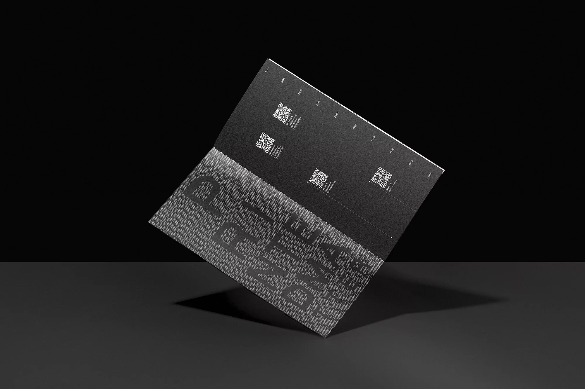 Open matte black brochure featuring QR codes and typographic design against a dark gradient background in a studio setting.