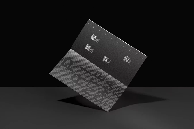 Open matte black brochure featuring QR codes and typographic design against a dark gradient background in a studio setting.
