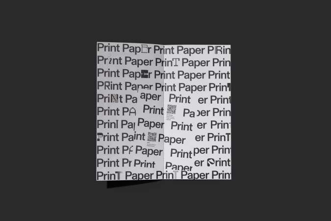Open white brochure with a repeating pattern of the words 'Print' and 'Paper' in black, against a solid dark gray background.