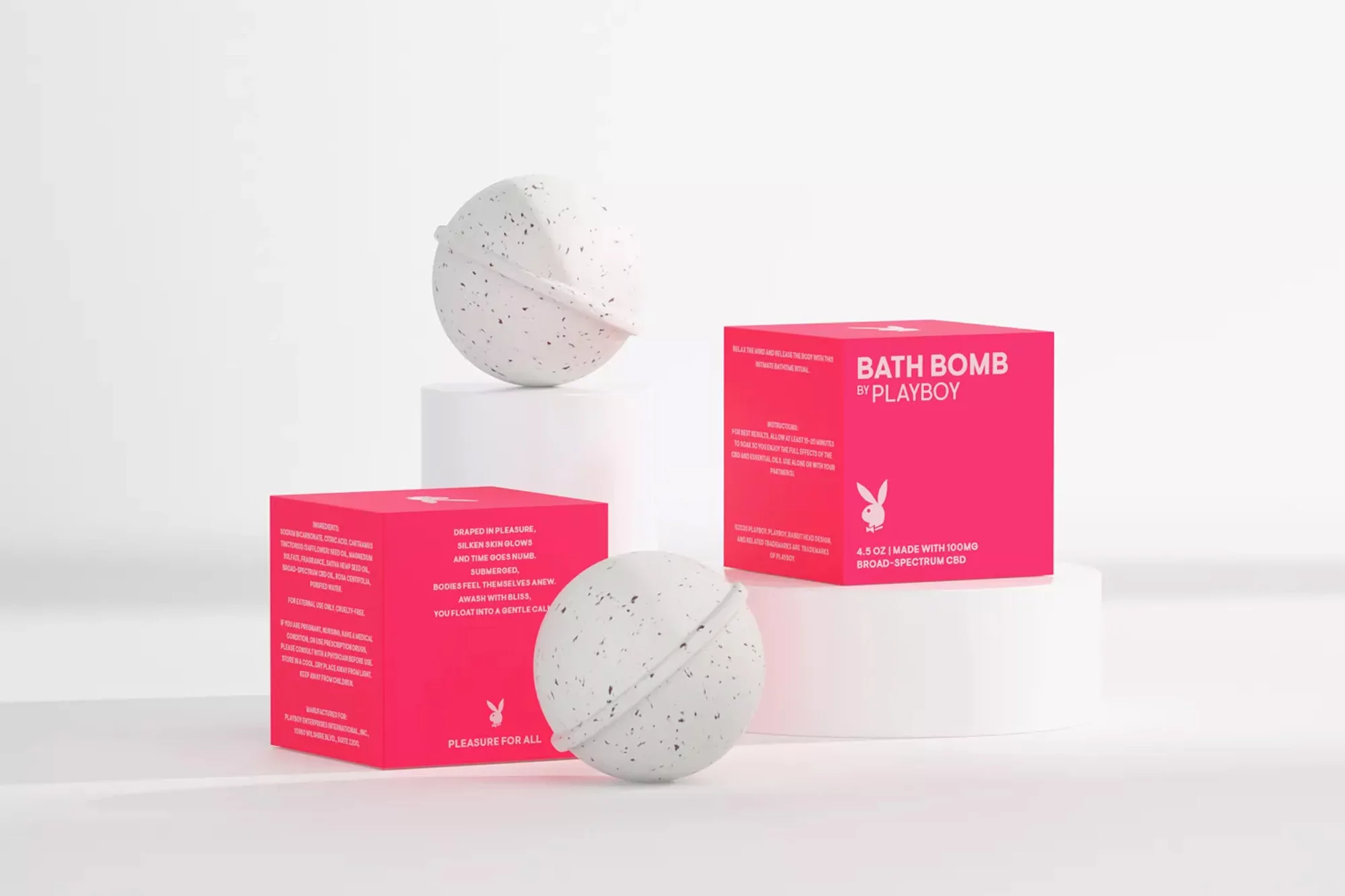 Product shot of bath bombs in speckled gray and pink packaging by Playboy, set against a clean, bright white background with geometric platforms.