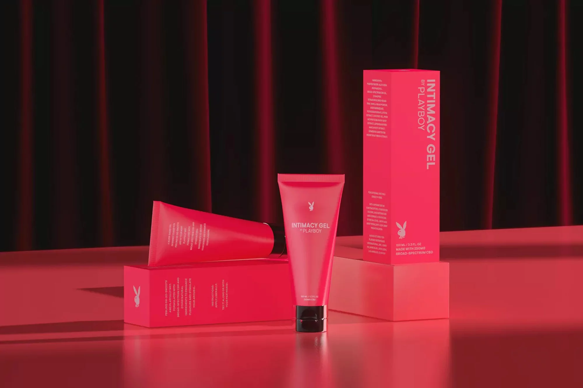 Product shot of Playboy Intimacy Gel featuring tube and box against a dark backdrop with subtle red lighting and minimal props.